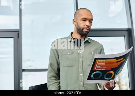 disabled man standing confidently in front of a desk, holding charts in a corporate office setting. Stock Photo