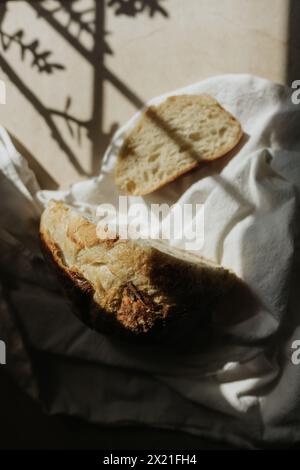 Freshly cut loaf of sourdough sitting on white tea towel in sunshine Stock Photo