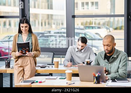 A diverse group of business professionals sitting around a table, engaged in a meeting using a laptop to work on a project. Stock Photo
