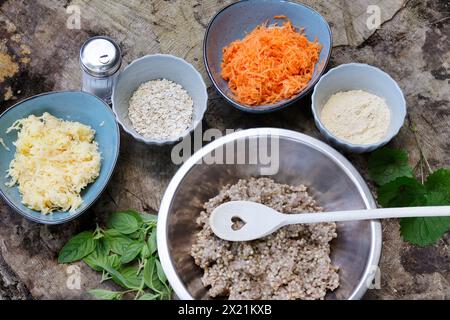 Making vegan herb patties, step 1: Ingredients; cooked buckwheat, fresh wild herbs, grated potatoes, grated carrots, chickpea flour, fine rolled oats, Stock Photo