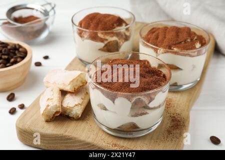 Delicious tiramisu in glasses, cookies and coffee beans on white table, closeup Stock Photo