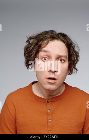 Vertical medium closeup studio portrait of surprised young Caucasian man with curly hair looking at camera, copy space Stock Photo