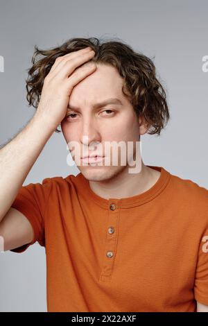 Vertical medium closeup studio portrait of young Caucasian man feeling annoyed posing for camera with hand on his head Stock Photo