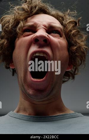 Low angle closeup studio portrait of enraged young Caucasian man with curly hair yelling Stock Photo