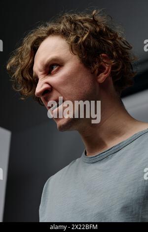 Vertical medium closeup studio portrait of young Caucasian man with curly hair expressing rage Stock Photo