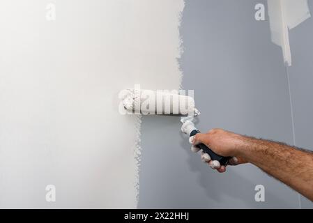 Painter paints a room in beige color using a paint roller at home. Stock Photo