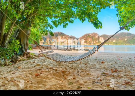 Romantic empty cozy bamboo hammock in the shadow of the trees jungle forest palm on the tropical beach sea with rocks in the bay... Stock Photo