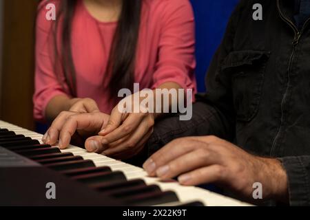 Unrecognizable Latin American teacher teaches and corrects the posture for playing the piano keyboard. Concept of music lessons Stock Photo