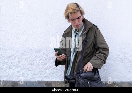Young Latin American man on the street checking his shoulder bag, holding cell phone Stock Photo