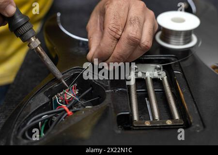 Latin American luthier's hands soldering with a soldering iron and tin the wires of the microphone system of an electric guitar. Unrecognizable person Stock Photo