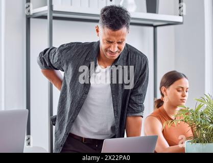 Office, desk and man with back pain, laptop and burnout in coworking space or design agency. Stress, posture and creative businessman with spine Stock Photo
