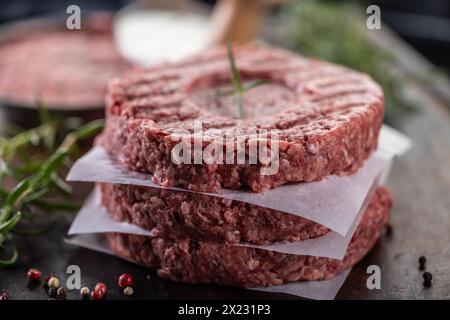 Fresh raw ground beef patties with rosemary salt and pepper made in a meat form on a cutting board. Stock Photo