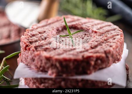 Fresh raw ground beef patties with rosemary salt and pepper made in a meat form on a cutting board. Stock Photo