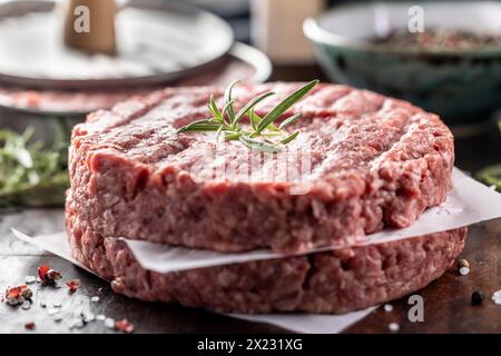 Fresh raw ground beef patties with rosemary salt and pepper made in a meat form on a cutting board. Stock Photo
