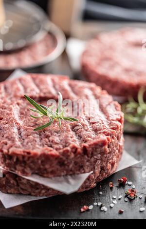 Fresh raw ground beef patties with rosemary salt and pepper made in a meat form on a cutting board. Stock Photo