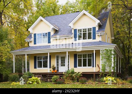 Two story yellow clapboard with blue and white trim cottage style home facade in autumn, Quebec, Canada Stock Photo