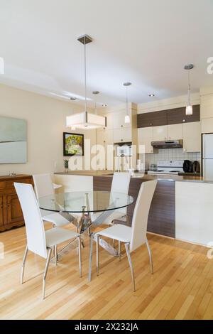 Dining room with round glass table, white leather high -back chairs and kitchen inside a renovated ground floor apartment in an old residential Stock Photo