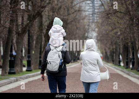 Couple with child walking on a city street in spring. Father with kid sitting on his shoulders Stock Photo