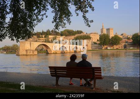 Couple on a park bench on the banks of the Rhone, Pont Saint Benezet bridge, Palais des Papes and Notre-Dame des Doms cathedral, Avignon, Vaucluse Stock Photo