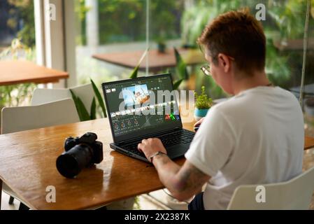Pro videographer edits wildlife footage on laptop in a bright office. Color grading process by creative with camera gear beside. Concentrated Stock Photo