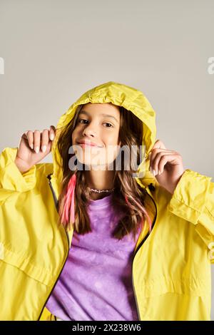 A stylish teenage girl poses actively in a bright yellow raincoat, exuding vibrancy and energy on a sunny day. Stock Photo