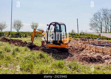 Excavator digging trench in soil for pipeline during building private house. Machinery for construction. Piping by foundation Stock Photo