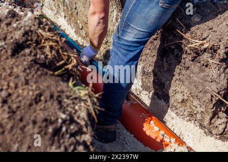 Plumber measuring slope of assembled sewage pipes using spirit level in trench. Building house. Worker checking pipeline Stock Photo