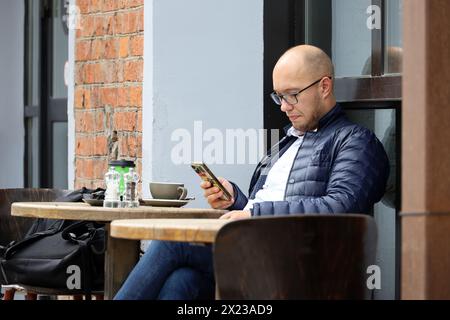 Man in eyeglasses sitting with smartphone in street cafe Stock Photo