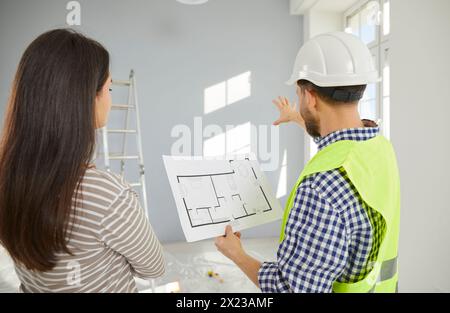 Architect, engineer or builder in uniform and helmet discusses construction plan with house owner Stock Photo