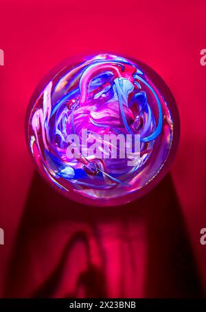 Colourful Glass Crystal Paperweight on a red background, with swirl pattern in a round ball shape. Concept of crystal Ball and fortune telling Stock Photo
