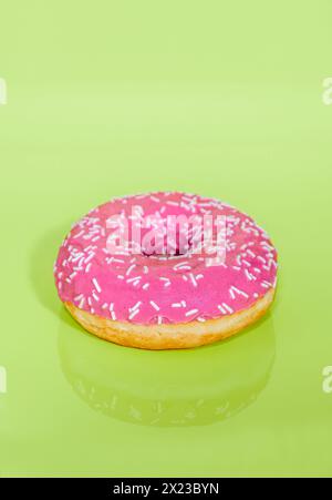 Pink iced Ring Doughnut on light green background with sprinkles on Stock Photo