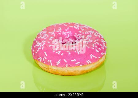 Pink iced Ring Doughnut on light green background with sprinkles on Stock Photo