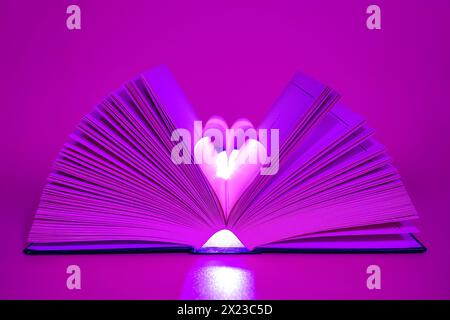 Open Book on pink/purple coloured background with middle pages turned into a heart shape Stock Photo