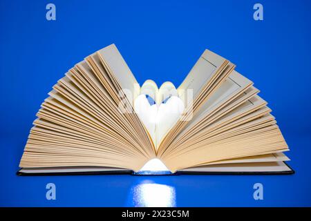Open Book on blue coloured background with middle pages turned into a heart shape Stock Photo