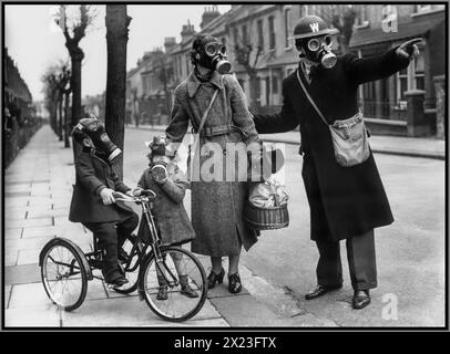WW2 GAS MASKS PROTECTION UK Street warden UK wearing a helmet and gas mask, in a suburban street directing a mother and her young children also wearing gas masks to an assembly point for practice gas attack . Britain UK 1940s World War II Second World War Stock Photo