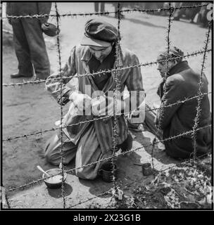 Liberation of Bergen-Belsen Concentration camp by British 11th Armoured Division, from Nazi Germany occupation April 1945 World War II Second World War WW2 with camp inmate behind barbed wire, wearing striped camp uniform, struggling with the meagre dry bread rations previously handed out by the brutal Nazi camp personnel regime. Stock Photo