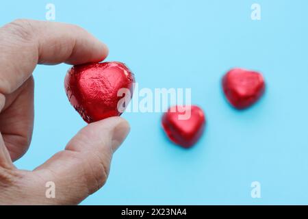 A close-up of a man's holds a red candy in the shape of a heart on a blue background. Stock Photo