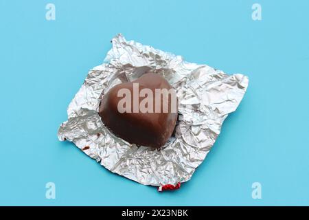 Chocolate candy and foil wrapper on a blue background..Close-up of an unwrapped candy. Stock Photo