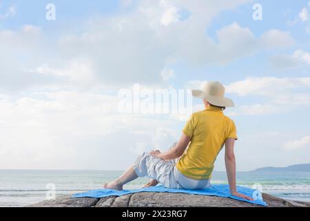 Woman sitting on a rock on the beach, Bombinhas, Santa Catarina, Brazil Stock Photo
