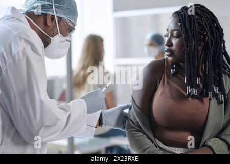 Side view of doctor giving vaccination shot to African American woman in clinic copy space Stock Photo