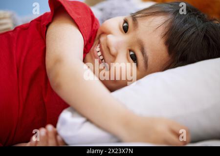 Smile, cute and boy child on bed playing and having fun at home with positive, good and happy attitude. Laughing, funny and sweet Asian kid relaxing Stock Photo