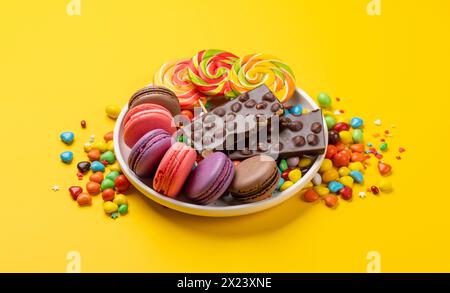 Various colorful candies, lollipops, and macaroons. Over yellow background Stock Photo