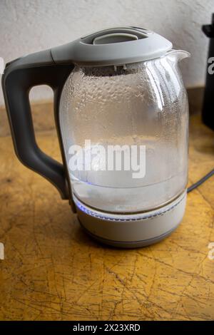 Glass electric kettle boiling water with a gray plastic handle.Domestic kitchen. Water to make tea or coffee. Stock Photo