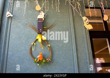 Easter street decor with carved wooden toys and garland. A wreath of willow branches stylized as an egg hangs on the wall of a house. Easter holiday. Stock Photo