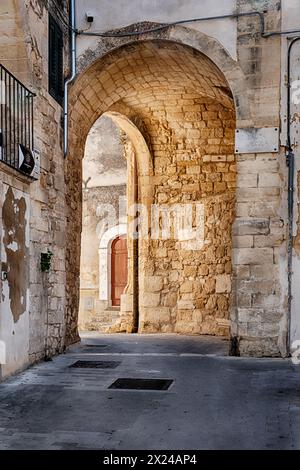 A stone archway in the old city of Ragusa allows sunlight to stream through and illuminate a narrow street. Stock Photo