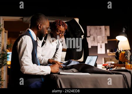 African american tailors working with premium quality fabrics in atelier shop workspace. Happy fashion designers making exquisite garments following sketch designs of upcoming bespoken collection Stock Photo