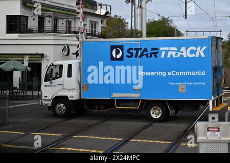 Side view of a blue and white Startrack delivery truck, as the vehicle crosses the Church St level crossing, on an overcast day Stock Photo