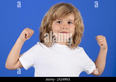 Cute child showing muscles on blue studio isolated background. Power kids. Kid boy showing strong fists. Stock Photo