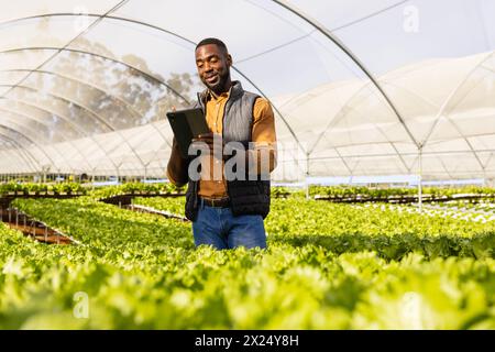 African American young male farmer holding a tablet among green plants in a greenhouse Stock Photo