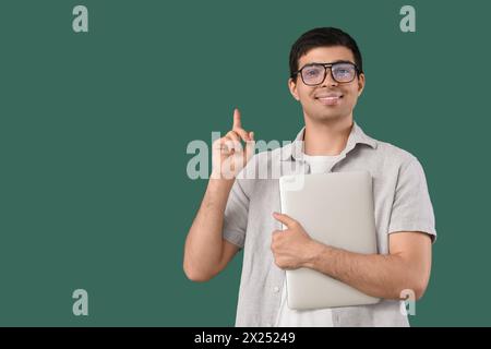 Male programmer with laptop pointing at something on green background Stock Photo
